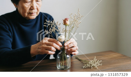 Elderly asian woman carefully arranging dried flowers in a glass vase on a wooden table 131857329