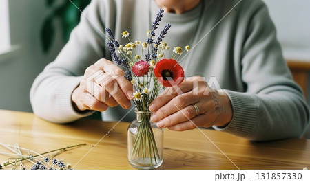 Senior woman hands carefully arranging a delicate dried flower bouquet in a glass vase Senior woman hands carefully arranging a delicate dried flower bouquet in a glass vase 131857330