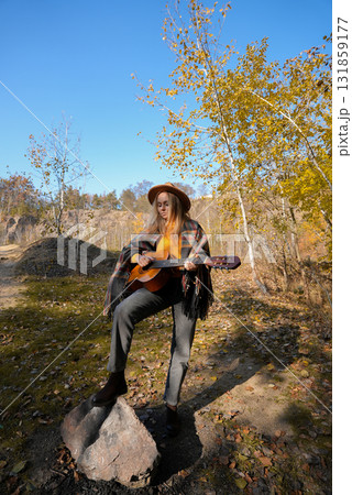 Portrait of smiling caucasian artist plays wooden acoustic guitar in autumnal park. Young songwriter plays string musical instrument hobby outside in nature fall time. Audio music healing Portrait of smiling caucasian artist plays wooden acoustic guitar in autumnal park. Young songwriter plays string musical instrument hobby outside in nature fall time. Audio music healing 131859177