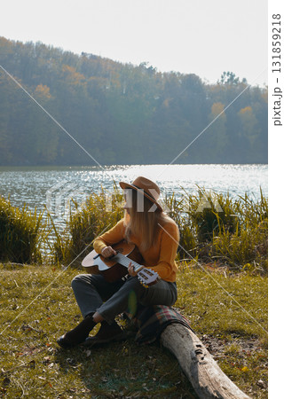 Beautiful blonde girl playing acoustic guitar and singing relaxing enjoying outdoors on sunny autumn day. Hippie woman in boho style learning and practicing playing musical instrument. Fall leaves Beautiful blonde girl playing acoustic guitar and singing relaxing enjoying outdoors on sunny autumn day. Hippie woman in boho style learning and practicing playing musical instrument. Fall leaves 131859218