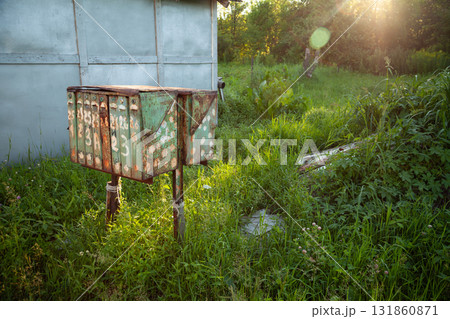 An old, rusty postbox stands weathered in a quiet Russian village, surrounded by green grass. A group of worn metal mailboxes with peeling paint in the countryside 131860871