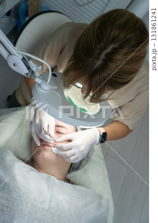 Dermatologist Facial Treatment Clinic Magnifying Lamp: Professional skin examination using a magnifying lamp during a facial treatment at a clinic. Dermatologist Facial Treatment Clinic Magnifying Lamp: Professional skin examination using a magnifying lamp during a facial treatment at a clinic. 131861241