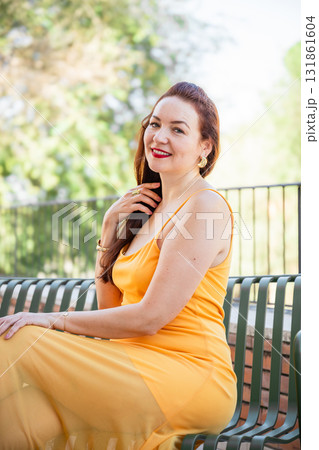 Woman in yellow dress sitting on bench outdoors and smiling 131861604