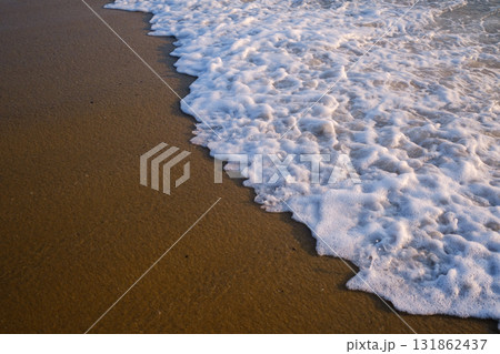 Gentle waves wash over golden sand during sunset on a tranquil beach in a coastal location, creating a serene environment for relaxation and reflection 131862437