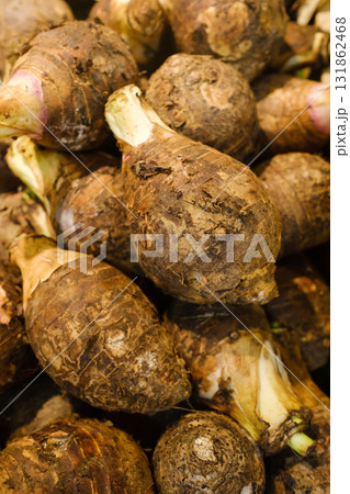 Fresh taro roots stacked together at a local market, showcasing their earthy textures and vibrant skin during a busy morning in a tropical region Fresh taro roots stacked together at a local market, showcasing their earthy textures and vibrant skin during a busy morning in a tropical region 131862468