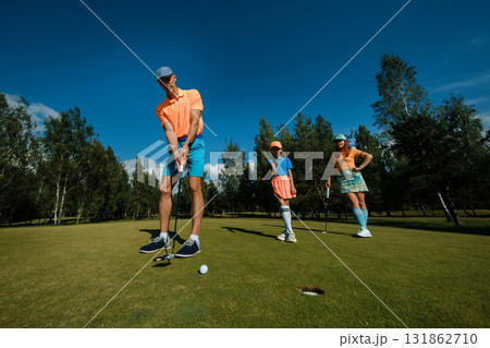 Family enjoys a fun day of golfing together on a sunny afternoon at a beautiful green course surrounded by trees Family enjoys a fun day of golfing together on a sunny afternoon at a beautiful green course surrounded by trees 131862710