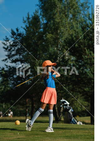Young girl practicing golf swing on a sunny day at the green park surrounded by trees, showcasing focus and enthusiasm for the sport 131862726