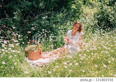 Daisy picnic woman, relaxing in field, summer. Lady enjoys wildflowers, basket, blanket, sunlit meadow. Peace. Daisy picnic woman, relaxing in field, summer. Lady enjoys wildflowers, basket, blanket, sunlit meadow. Peace. 131863558