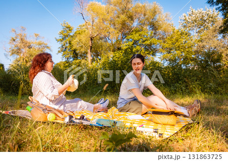 Two women reacting to itchy bug bites while lying on picnic blanket in city park during hot summer afternoon outdoors. Low angle view 131863725