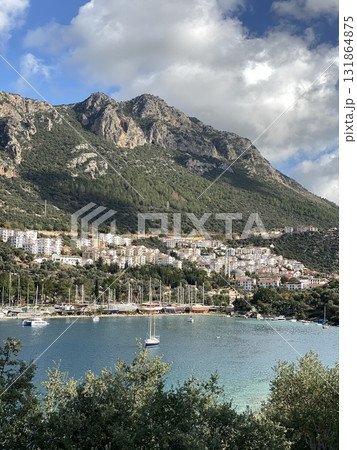 Coastal mountain town with sailboats in harbor under partly cloudy sky, ideal for travel background 131864875