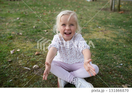 Little 4 year old blonde girl sitting on the grass and laughing 131866870