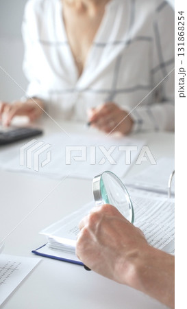 Groupe of professional accountants working together, using a magnifying glass and a calculators, to audit financial reports in their brightly lit office. Audit and taxes concept 131868254