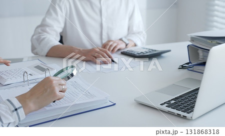 Team of accountants are working together, using a magnifying glass and a calculator, to audit financial reports in office. Audit and taxes in business 131868318