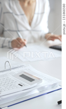 Close up of a calculator on financial documents, with an accountant taking notes, emphasizing accounting, finance, and tax preparation. Audit and taxes in business Close up of a calculator on financial documents, with an accountant taking notes, emphasizing accounting, finance, and tax preparation. Audit and taxes in business 131868380