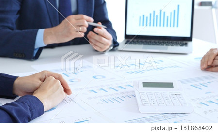 Business people collaborating at a conference table, reviewing financial charts and reports, using a laptop and calculator while engaging in discussions about strategy and performance. Accouters at 131868402