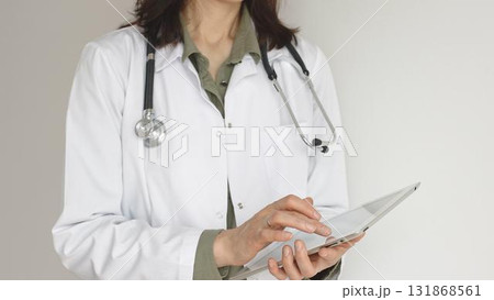 Unknown professional woman doctor, wearing white coat over a green blouse and a stethoscope, is using a digital tablet, suggesting innovative healthcare practices in medicine. Health care concept 131868561