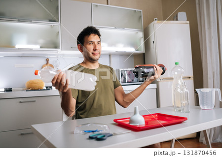 Professional gardener blending organic fertilizers in plastic bottle, preparing nutrient solution near kitchen windowsill with gardening supplies and potted plants nearby. Concept of home gardening. Professional gardener blending organic fertilizers in plastic bottle, preparing nutrient solution near kitchen windowsill with gardening supplies and potted plants nearby. Concept of home gardening. 131870456