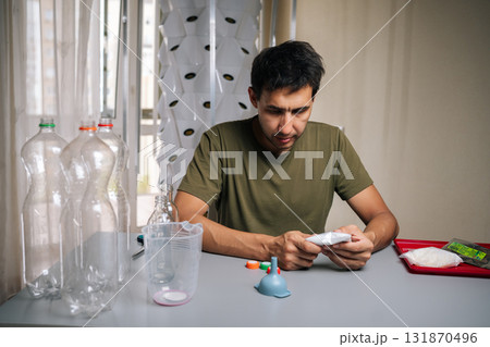 Home gardener sitting at table preparing to mixing fertilizer from recycled bottles for innovative vertical garden setup, emphasizing eco-friendly urban agriculture. Concept of indoor farming. Home gardener sitting at table preparing to mixing fertilizer from recycled bottles for innovative vertical garden setup, emphasizing eco-friendly urban agriculture. Concept of indoor farming. 131870496