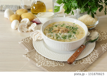 Tasty champignon mushrooms soup with cream and cheese in white bowl on white wooden background 131870823
