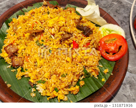 Fried rice with meat and vegetables, served on a banana leaf and clay plate. Traditional Indonesian culinary. Fried rice with meat and vegetables, served on a banana leaf and clay plate. Traditional Indonesian culinary. 131871916