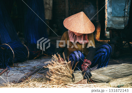 Vietnamese woman in traditional straw hat Non La cuts reeds at a woven mat factory in village in Vietnam 131872143