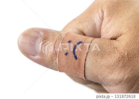 Thumb wrapped in bandage with sad face drawn on it, conveying sense of injury or discomfort. close up image highlights texture of skin and bandage 131872618
