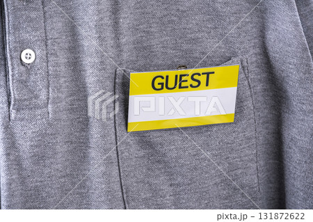 Guest badge with yellow border is clipped to pocket of gray shirt, indicating visitor status. badge stands out against fabric, suggesting formal or organized event 131872622