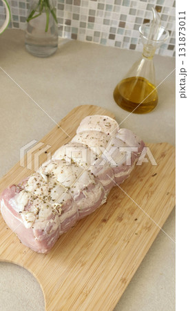 Pork tenderloin tied with rope on wooden board. Spices and cooking meat at home in kitchen. 131873011