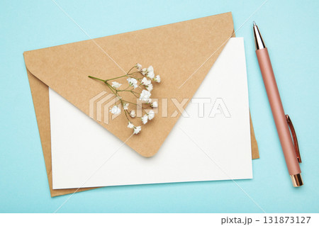 Craft envelope with paper card, pen and white gypsophila flowers on pastel blue background. Space for text 131873127