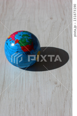 A vertical photo of a globe with the American continents visible in the light and its shadow cast on a wooden plank. An illustrative photo for the theme of light and time zones on different continents 131873190