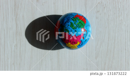 A top view of the North Pole on a colored globe that casts a textured shadow on a wooden surface. Conceptual photo illustrating different times of day on planet Earth 131873222