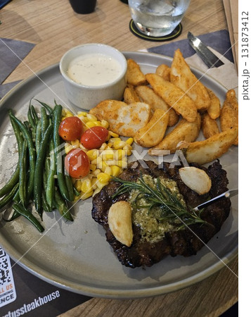 A delicious grilled steak is beautifully plated with roasted garlic, a sprig of rosemary, a side of golden potato wedges, steamed green beans, sweet corn, and bright cherry tomatoes, A delicious grilled steak is beautifully plated with roasted garlic, a sprig of rosemary, a side of golden potato wedges, steamed green beans, sweet corn, and bright cherry tomatoes, 131873412