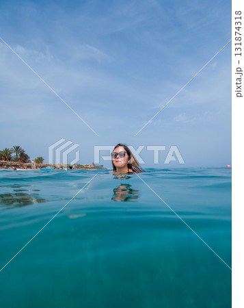 A young woman with sun glasses swimming in the blue sea. A blue hazy sky in the background A young woman with sun glasses swimming in the blue sea. A blue hazy sky in the background 131874318
