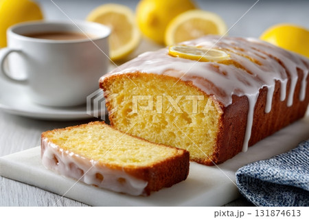 Homemade lemon drizzle cake with icing. Classic lemon pound cake with citrus glaze and zest. Whole loaf, side view, close up. Fresh homemade baked dessert with lemon slices. Blurred tea set background Homemade lemon drizzle cake with icing. Classic lemon pound cake with citrus glaze and zest. Whole loaf, side view, close up. Fresh homemade baked dessert with lemon slices. Blurred tea set background 131874613