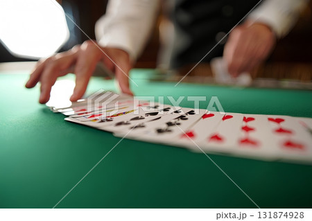 Casino dealer in white shirt dealing cards on a green felt table, close-up action shot of a professional poker game in progress 131874928
