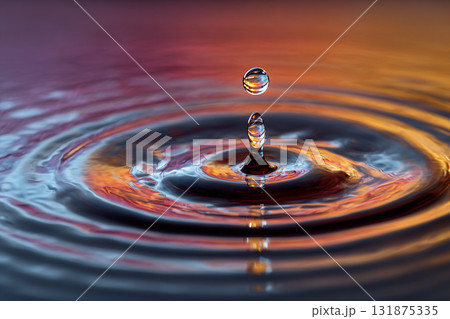 A single water droplet is suspended mid-air above the surface, creating a perfect column and vibrant ripples reflecting warm orange and purple light. A single water droplet is suspended mid-air above the surface, creating a perfect column and vibrant ripples reflecting warm orange and purple light. 131875335
