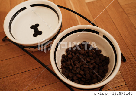 Two ceramic bowls for pet food and water on a wooden parquet floor, minimalist setup with warm indoor lighting. Pet care concept Two ceramic bowls for pet food and water on a wooden parquet floor, minimalist setup with warm indoor lighting. Pet care concept 131876140