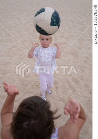 Mother teaching her 4-year-old daughter to play volleyball on the beach  131876349