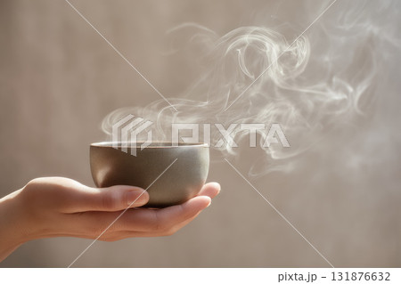 Hand holding ceramic cup with hot beverage, steam rising in soft natural light, minimalist modern style, calm and peaceful atmosphere, close up studio photo 131876632