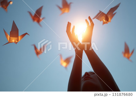 Hands reaching towards sunlight with origami cranes flying in sky, symbolizing hope, freedom, and inspiration in minimal surreal style 131876680