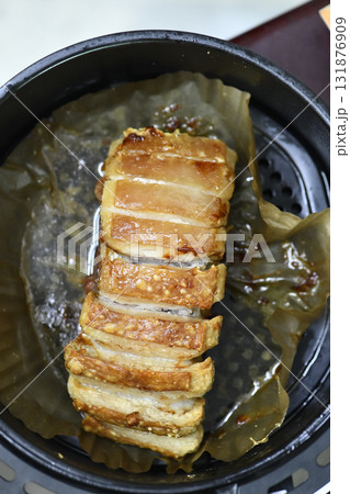 Roasted pork belly slices with crispy crackling on parchment in round pan, savory golden brown and glistening with juices Roasted pork belly slices with crispy crackling on parchment in round pan, savory golden brown and glistening with juices 131876909
