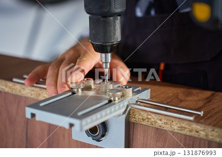 Carpenter drilling wooden panel using jig tool for precise holes 131876993