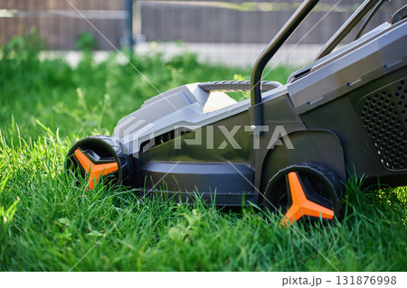Electric lawn mower cutting green grass in backyard 131876998