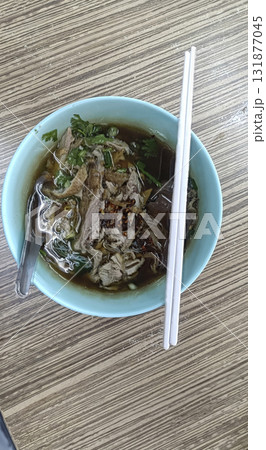 Shredded beef noodle soup in ceramic bowl with chopsticks and spoon, savory broth and fresh herbs, comforting street food meal Shredded beef noodle soup in ceramic bowl with chopsticks and spoon, savory broth and fresh herbs, comforting street food meal 131877045