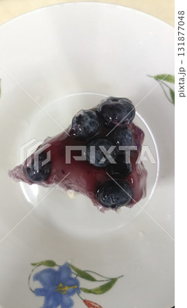 Blueberry topping cheesecake slice white plate with floral pattern, glossy fruit glaze and creamy texture, appetizing dessert presentation 131877048