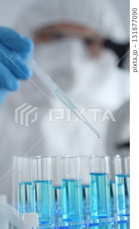 Close up of scientific researcher or virologist wearing protective gear, carefully pipetting liquid into test tubes in laboratory. Medicine, healthcare and science concept Close up of scientific researcher or virologist wearing protective gear, carefully pipetting liquid into test tubes in laboratory. Medicine, healthcare and science concept 131877090