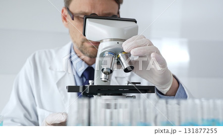 Scientific researcher wearing lab coat, glasses and white protective gloves carefully calibrating laboratory microscope, performing precision medical investigation. Medicine, healthcare and science 131877255