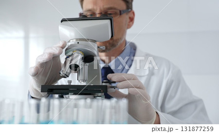 Scientific researcher wearing lab coat, glasses and white protective gloves carefully calibrating laboratory microscope, performing precision medical investigation. Medicine, healthcare and science 131877259