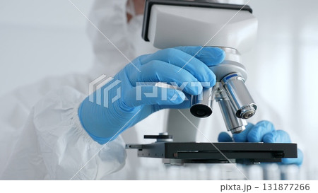Scientific researcher wearing blue protective gloves fine tuning microscope lenses during medical laboratory investigation. Medicine, healthcare and science concept Scientific researcher wearing blue protective gloves fine tuning microscope lenses during medical laboratory investigation. Medicine, healthcare and science concept 131877266