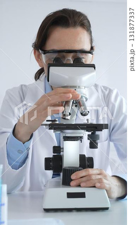 Female scientist wearing lab coat and protective glasses using microscope, analyzing samples in test tubes in laboratory, conducting scientific research Female scientist wearing lab coat and protective glasses using microscope, analyzing samples in test tubes in laboratory, conducting scientific research 131877337